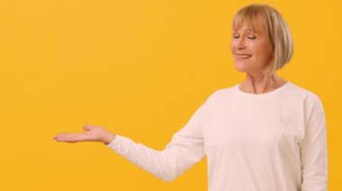 Beyaz bluzlu, gülümseyen bir kadın kolunu açık bir elle uzatıyor ve davetkar bir hareket sergiliyor. Parlak sarı arka plan onun sıcak tavrını ve neşeli ifadesini arttırır, boşluğu taklit eder.