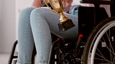 Tekerlekli sandalyede oturan bir insan, açık mavi kot pantolon giyiyor, kapalı bir ortamda, içinden doğal ışık akıyor. Atmosfer sessiz ve rahat görünüyor..