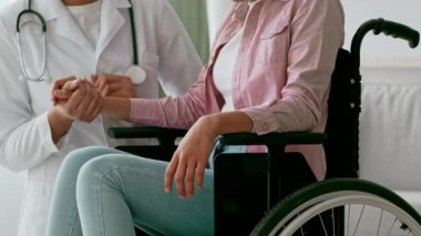 İlgili bir sağlık uzmanı tekerlekli sandalyedeki bir hastanın elini nazikçe tutuyor. Sağlık ziyareti sırasında sıcaklığı ve desteği aktaran kurulum, empatiyi vurguluyor.