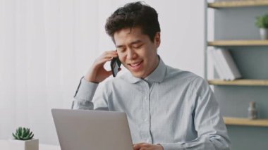 Bin yıllık bir adam dizüstü bilgisayarına odaklanmışken telefonuyla sohbet ediyor. Etrafı bitki ve kitaplarla çevrili, aydınlık, modern bir ev ofisinde, uzak çalışma hayatını gösteriyor..