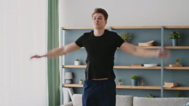 Sportif bir genç adam evde antrenman yapar. Forma ve sağlıklı bir yaşam tarzına olan bağlılığını gösterir. Parlak ve modern bir yaşam alanında egzersiz yapıyor..
