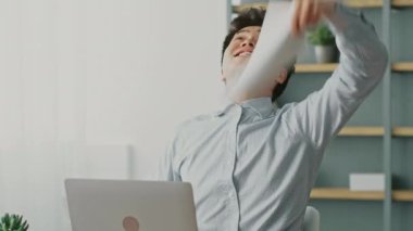 Genç bir Asyalı adam şık ev ofisinde uzaktan çalışırken zaferi sevinçle kutluyor. Etrafı yeşilliklerle çevrili, pozitif enerjiyle dolu verimli bir çalışma ortamı sergiliyor..