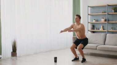 Genç, atletik bir adam modern evinde egzersiz yapıyor. Formda olduğunu gösteriyor. Açık alan iyi ışıklandırılmış, sağlıklı bir yaşam tarzının ve fitness 'e adanmışlığın altını çiziyor..
