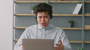 Bin yıllık bir adam, ev ofisinin masasında oturmuş kulaklık takarken dizüstü bilgisayarına odaklanmış halde. Arka planda raflarda bitki ve kitaplar duruyor, verimli bir atmosfer yaratıyor..