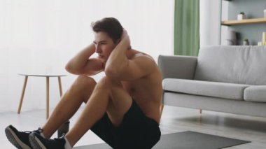Genç, sportif bir adam şık bir oturma odasında paspasın üzerinde egzersiz yapıyor. Spor yaparken sağlıklı yaşam tarzı seçimlerini vurgulayarak spor rutinine odaklanıyor..