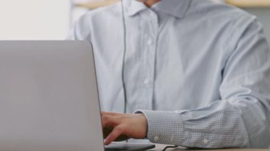 Genç bir Asyalı adam modern bir yurt ofisindeki işine odaklanıyor. Akıllı telefonu masanın üzerinde dururken dizüstü bilgisayarında daktilo kullanıyor. Ayarlar uzak ve rahat bir çalışma ortamını yansıtıyor.