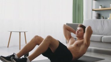 Sportif bir genç adam oturma odasındaki paspasın üzerinde egzersiz yapıyor, fitness ve refah üzerine odaklanıyor. Sağlıklı bir yaşam tarzına olan bağlılığı egzersiz rutininde açıkça görülüyor..