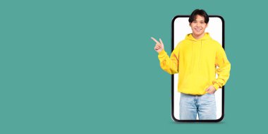 Sarı kapüşonlu genç bir adam yeşil arka planı olan büyük bir akıllı telefonun yanında duruyor ve çevrimiçi bir sohbete girişiyor. Odak noktası dijital etkileşim ve teknoloji..