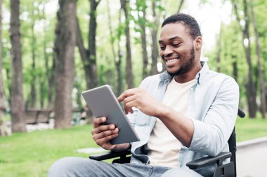 Tekerlekli sandalyedeki mutlu genç adam tablet bilgisayar kullanıyor, internette geziniyor ya da Spring Park 'ta film seyrediyor. Milenyum Afrikalı Amerikalı çocuk dışarıda sosyal medyayı kontrol ediyor.
