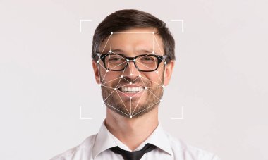 Yüz tanıma teknolojisi özelliklerini ön plana çıkarırken gözlüklü bir adam gülümsüyor. Boş alanla minimalistik ayarlar, yüz tanımlamasına odaklanmayı vurguluyor.