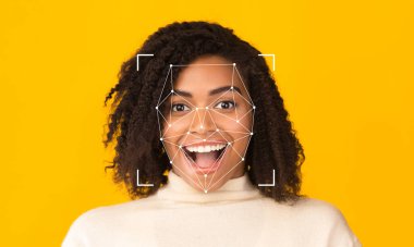 Kıvırcık saçlı bir kadın yüz tanıma teknolojisi özelliklerini tararken heyecanını ifade eder. Parlak sarı arka plan onun ifadesine ve iş yerindeki teknolojisine odaklanmamızı sağlıyor..