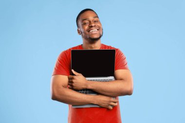 Harika bir site. Mavi Stüdyo Arkaplanı 'nda boş ekran pozu veren ve kameraya gülümseyen mutlu Afrikalı Amerikalı adam. Bilgisayar Kavramını Seviyorum. Teknoloji, İnsanlar ve Gadget