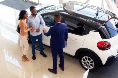 Araba galerisi. Otomobil Salonu 'nda başarılı bir anlaşmadan sonra müşterilerin en iyi görüntüsü: Çift ve Siyah Erkek Yönetici El sıkışması, Afro-Amerikan Eşler Şov Salonunda Lüks Otomobil Satın Alırken