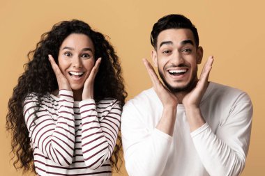 Harika bir teklif. Şaşırmış Arap çiftin portresi kameraya bakıyor ve heyecanla yüzlerine dokunuyor, Ortadoğulu eşlerin sarı stüdyo arka planında durmaları,