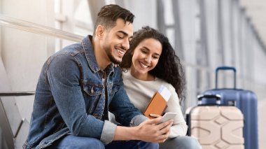 Uçuşu bekliyorum. Genç Arap Eşler Havaalanı Terminalinde Akıllı Telefon Kullanıyor, Orta Doğulu Çift Cep Telefonu 'nda İnternet Taraması Ya da Uçağa Binmeden önce İnternetten Otel Rezervasyonları, Kapalı Çekim