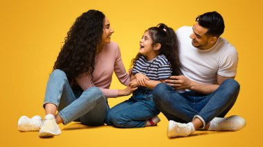 Mutlu bir Orta Doğulu aile stüdyoda sarı arka planda otururken eğleniyor, mutlu bir Arap ebeveyn kızıyla oynuyor, çocuklarını gıdıklıyor ve gülüyor, boş bir alan yaratıyor.