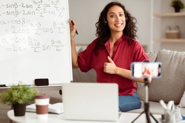 Bayan öğretmen çevrimiçi okulu tavsiye ediyor, işaret gösteriyor, sanal ders veriyor, matematiği anlatıyor. Eğitim hizmetlerinden memnun olan, cep telefonuyla video kaydeden,