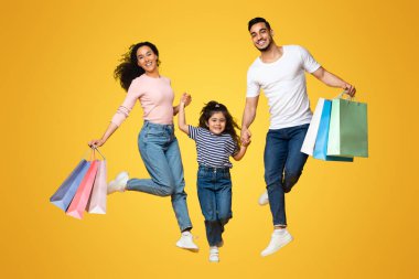 Büyük Alışveriş Konsepti. Üç kişilik neşeli bir Arap ailesi, bir sürü alışveriş çantası ile sarı stüdyo geçmişine atlıyorlar, Orta Doğulu aileler ve küçük kızları mevsimlik satışların keyfini çıkarıyorlar,