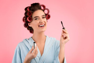 Göz makyajı. Kirpiklerine maskarası süren mutlu kadın, sarı stüdyo arka planında elbise giymiş kamera pozu vererek gülümsüyor. Kadın Dekoratif Kozmetik