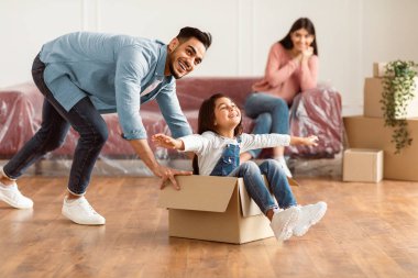 Taşındıkları gün yeni evlerinde eğlenen üç kişilik neşeli bir aile. Mutlu sakallı adam ve kızı hareket halindeyken karton kutuyla oynuyorlar.