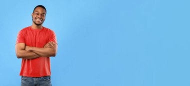 Gülümseyen Afro-Amerikalı adam kameraya gülümsüyor. Karşıdan karşıya geçerken mavi arka planda duruyor. Mutlu Özgüven Stüdyosu Siyahi Milenyum Adamı Pozitif Duygular İfade Ediyor