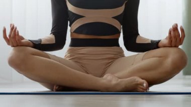 Genç bir Afrikalı Amerikalı kadın evinde yoga minderinin üzerinde bağdaş kurarak oturuyor, nefes alıp verişine ve meditasyonuna odaklanıyor. Günlük rutininde sağlık ve refahı kucaklıyor..