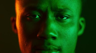 Yakışıklı bir milenyum adamı güçlü bir ifadeyle doğrudan kameraya bakıyor. Parlak yeşil neon renklerle aydınlatılıyor ve modaya uygun, modern bir ortamda kendi özelliklerini vurguluyor..