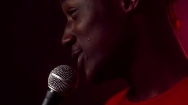 Etkileyici bir Afrikalı Amerikalı izleyiciyle canlı bir neon fona karşı mikrofon tutarken iletişim kuruyor..