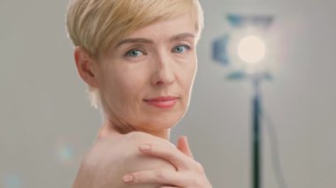 50 'li yaşlarında beyaz bir kadın yüzüne cilt ürünleri sürüyor. Kısa saçı, kendini şımartmaya odaklanırken rahat yüzünü çerçeveler..