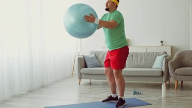 Bir adam evde egzersiz topuyla antrenman yapmaya başlar. Atletik kıyafetler giyiyor ve spor yolculuğuna odaklanıyor. Parlak ve havadar alan motive edici atmosferi arttırır..