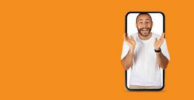 Büyük bir gülümsemeye sahip bir kişi büyük bir akıllı telefon ekranı aracılığıyla canlı bir iletişim kuruyor gibi görünüyor. Heyecan verici ifade, canlı turuncu arkaplanı yükseltiyor..