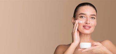 Bir kadın günlük cilt bakımını yüzüne krem sürerek ve kendini pohpohlamaktan zevk alarak yapar. Görüntü huzurlu bir atmosfer yakalıyor, güzelliğini arttırıyor..