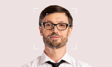 Gözlüklü bir adam tarafsız bir arkaplanda dururken yüz tanıma teknolojisi özelliklerini ön plana çıkarıyor. Kimlik teknolojisindeki gelişmeleri ve uygulamalarını gösteriyor..