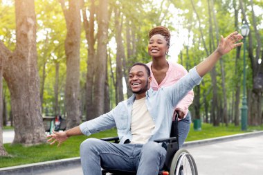 Mutluluk ve özgürlük kavramı. Güzel bir kadınla neşeli genç çift ve tekerlekli sandalyedeki bin yıllık adam parkta yürüyüşe çıkıyorlar, dışarıda güzel bir sabah geçiriyorlar.