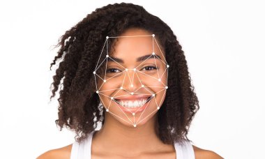 Kıvırcık saçlı bir kadın yüzünü tarayan yüz tanıma teknolojisiyle gülümsüyor..