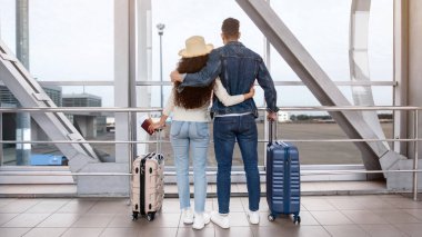 Havalimanı Terminali 'nde pencereden dışarı bakan romantik bir çiftin arka görüntüsü, tanınmayan eşler yaz tatiline hazır, bavullarıyla ayakta duruyor, kucaklıyor, birlikte seyahat ediyor, uzayı kopyalıyor.