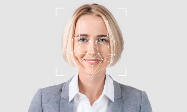 Sarışın bir kadın, yüz tanıma teknolojisi özelliklerini incelerken kendine güvenerek gülümsüyor. Ayar, konuyu ve teknolojiyi vurgulayan, ışık ve boş bir arkaplana sahiptir..