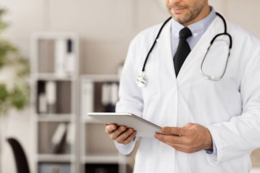 Tıbbi bakım ve teknoloji konsepti. Dijital tablet kullanan tanınmayan pratisyen hekimin klinikteki ya da hastanedeki ofisinde dikilmesi. Boşluğu kopyala, arkaplanı bulanıklaştır