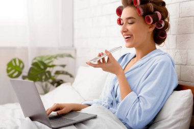 Neşeli, Çekici Kadın, cep telefonunda sesli arama uygulaması kullanıyor ve bilgisayarla modern yatak odasında çalışıyor. Mobil Teknoloji ve İletişim, IOT kavramı. Yan Görünüm