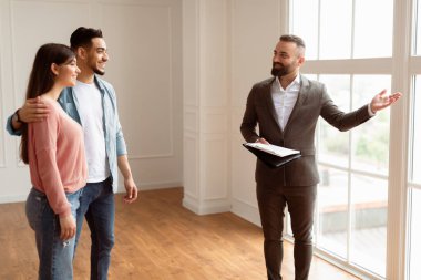 Profesyonel emlakçı genç bir Arap çifte yeni bir daire gösteriyor, büyük kattan tavana kadar güzel bir manzaraya bakıyor ve işaret ediyor. Mutlu Adam ve Bayan Satıcıyla Konuşuyor