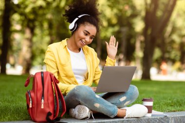 Mesafe iletişimi. Yeşil Park 'ın dışında oturan Afrikalı Amerikalı Öğrenci Bilgisayarı kullanarak Bilgisayarı Arıyor ve Uzaktan Öğrenme Dersini İzliyor. Modern Çevrimiçi Eğitim