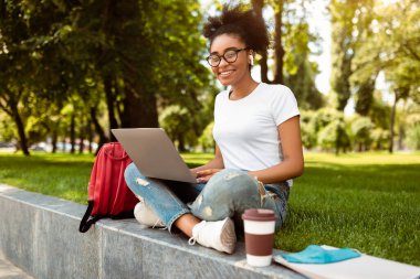 Uzaktan Öğrenme. Laptop kullanan, kulaklık takan, kampüs parkında kameraya gülümseyen mutlu siyah kız öğrenci. Uzaklık E-Öğrenme, Modern Eğitim Konsepti