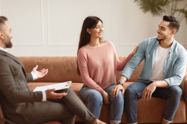 Çift Terapisi Konsepti. Mutlu karı koca seansta terapist ofisinde uzlaşıyorlar, birbirlerine bakıyorlar, gülümseyen kadın erkeğin omzuna dokunuyor, kanepede oturuyorlar.