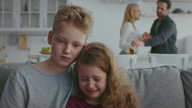 İki çocuk bir kanepede birbirine sarılıyor. Evlerinde aile içi şiddet baş gösterirken korku ve üzüntü gösteriyorlar..