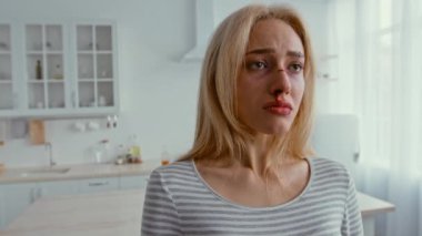 Parlak bir mutfakta duran bir kadın, gözle görülür şekilde sıkıntılı ve gözyaşı dolu. Atmosfer, altında yatan iç çatışma ve duygusal karışıklığı gösteriyor..