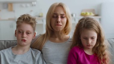 İki çocuk bir kadının yanında oturuyor, hepsi de sıkıntı belirtileri gösteriyor. Oda modern dekor, aile dinamiklerini etkileyen iç sorunlara işaret ederek ifadeleriyle çelişiyor..