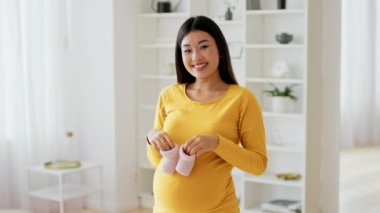 Neşeli bir Asyalı, güneşli bir oturma odasında pembe bebek poposu tutarken annesinin gülümsemesini bekliyor. Doğal ışık boşluğu doldurur, neşeli anı için sıcak ve misafirperver bir atmosfer yaratır..