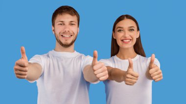 Hoşumuza gitti. Mutlu çift başparmaklarını sallıyor ve gülümsüyor. Pastel mor stüdyo duvarında izole edilmiş.