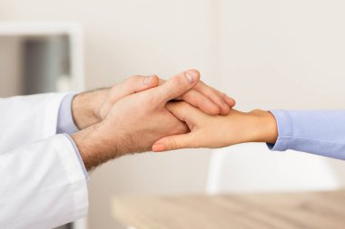 Empati ve Cesaret Konsepti. Kadın hastayı rahatlatan erkek doktorların yakın çekimleri. Hastanedeki muayenehanesinde el ele tutuşmaları. Pratisyen hekim genç hasta bayana tezahürat yapıyor.