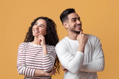 Dalgın Arap erkek ve kadın bir şey düşünüyor ve uzaklara bakıyor, düşünceli orta doğu çifti çenelerine dokunuyor ve sarı arka planda birlikte poz verirken gülümsüyor,